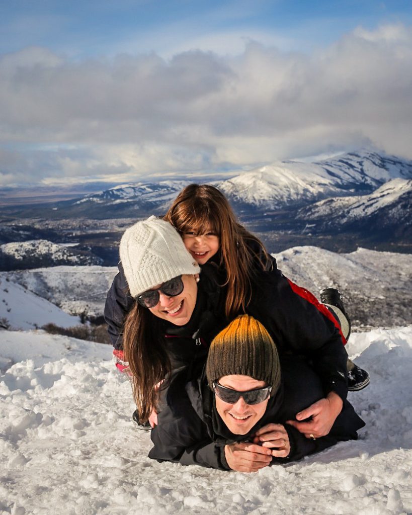Foto divertida de família deitada com fundo de neve e montanhas