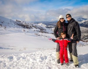 familia com mãe, pai e filha pequena em paisagem de neve com montanha ao fundo