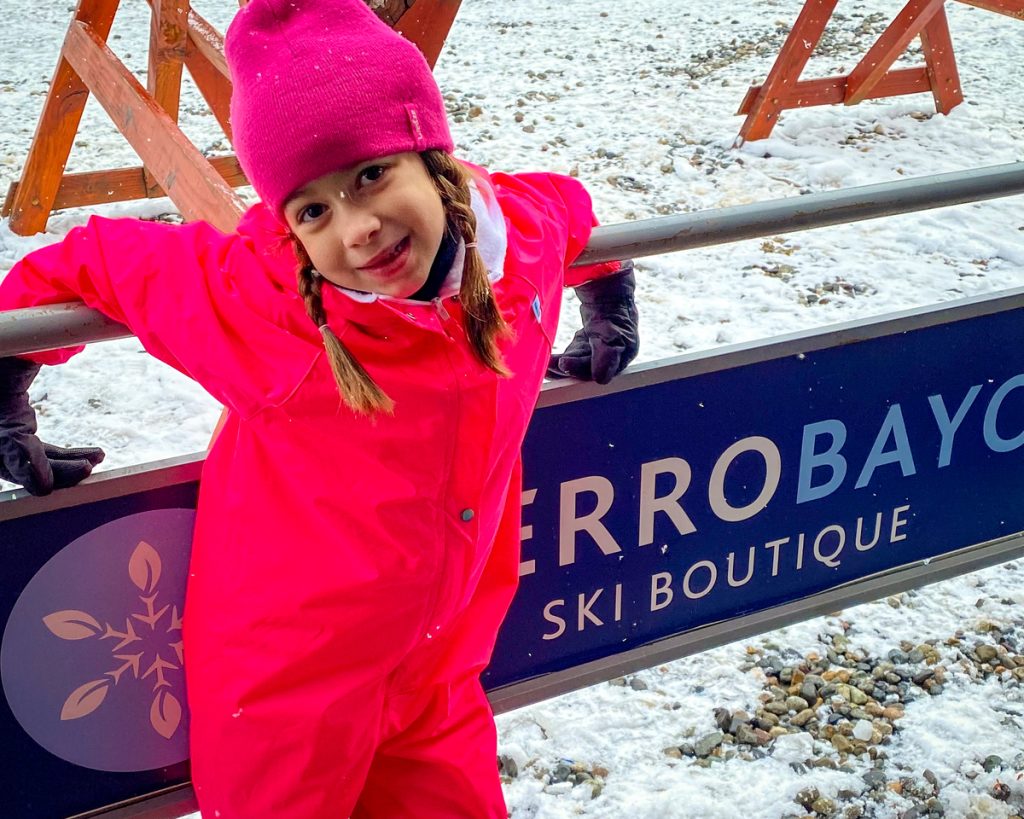Menina sorrindo debruçada em placa na neve