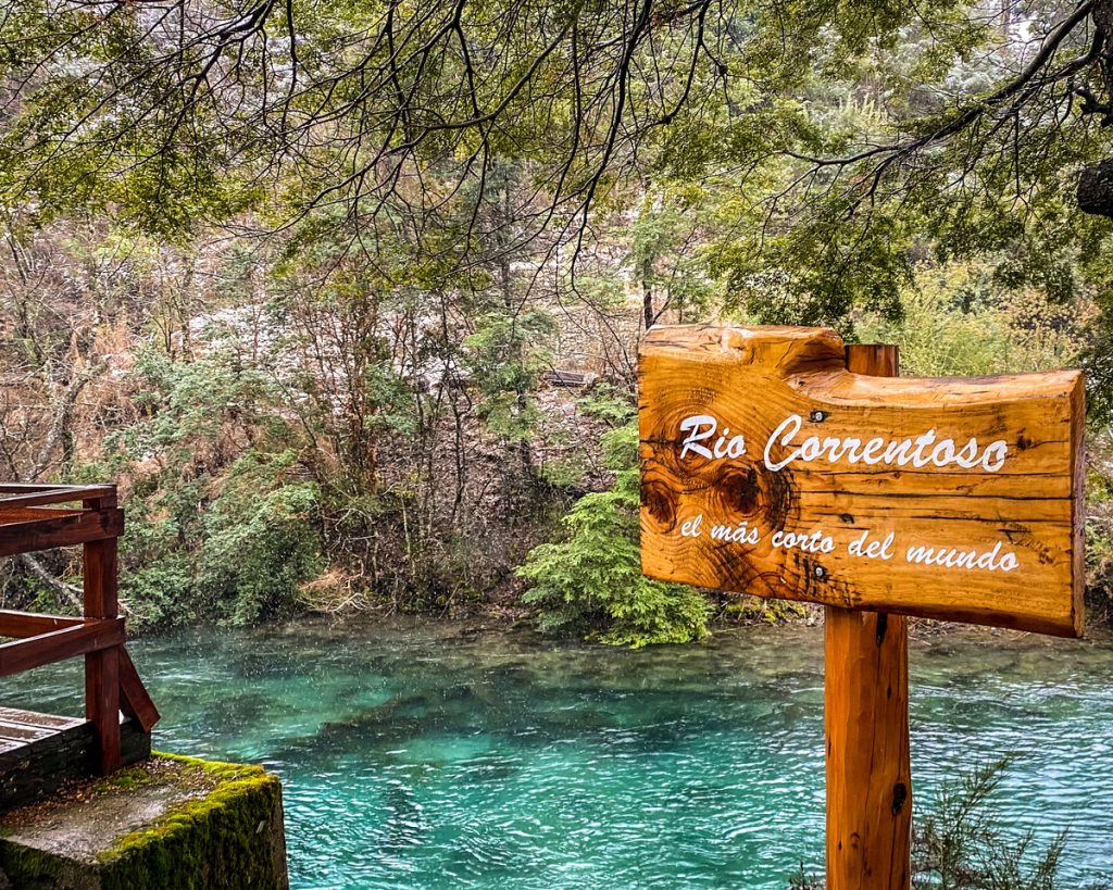 Placa de madeira de identificação com rio azulado e vegetação