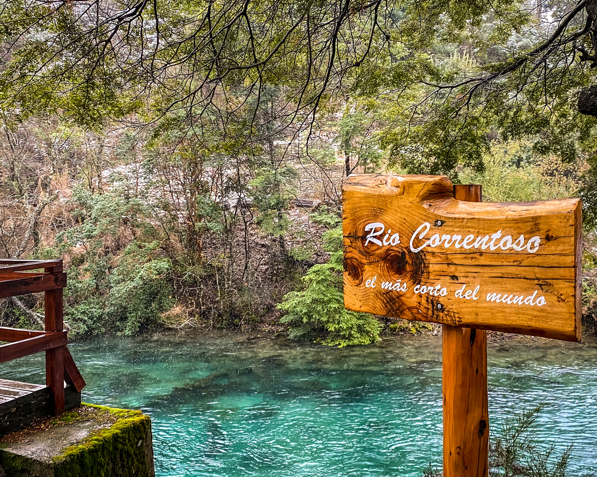 Placa de madeira de identificação com rio azulado e vegetação