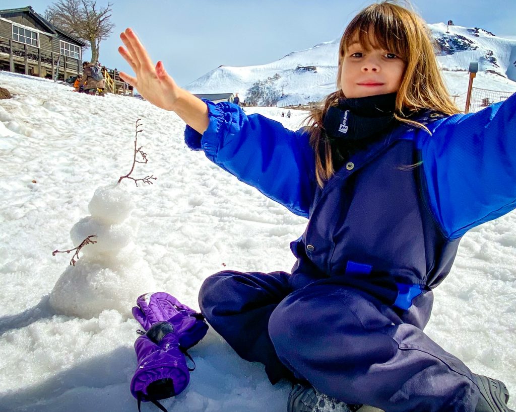 menina de braços abertos sentada na neve