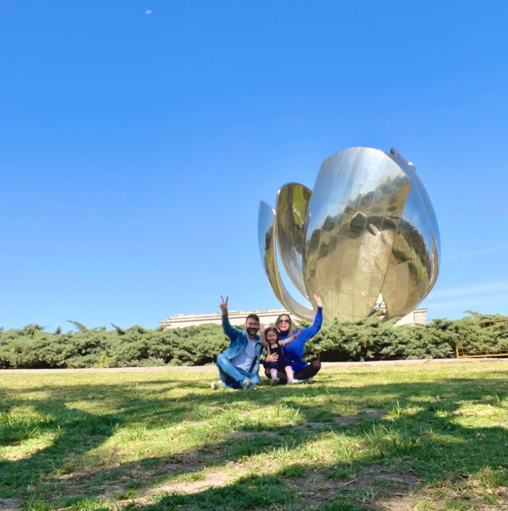 Família sentada em gramado em frente a escultura Floralis Generica