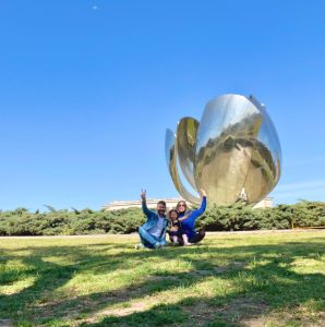 Família sentada em gramado em frente a escultura Floralis Generica