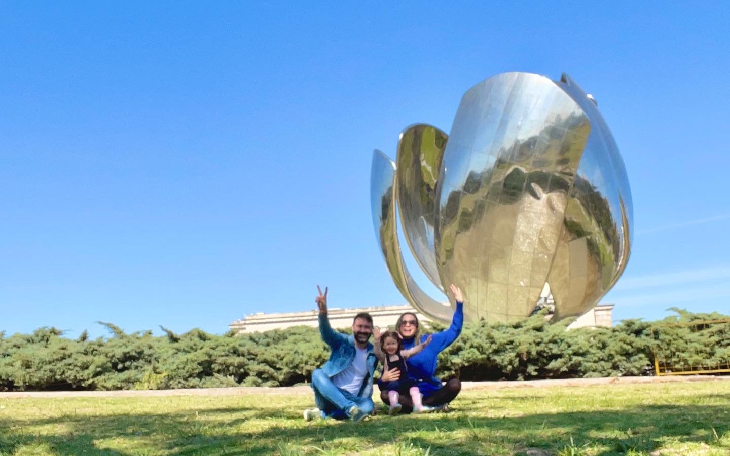 Família sentada em gramado em frente a escultura Floralis Generica