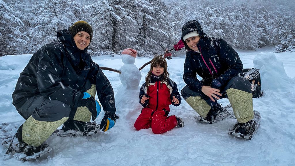 familia abaixada com pequeno boneco de neve e chão nevado