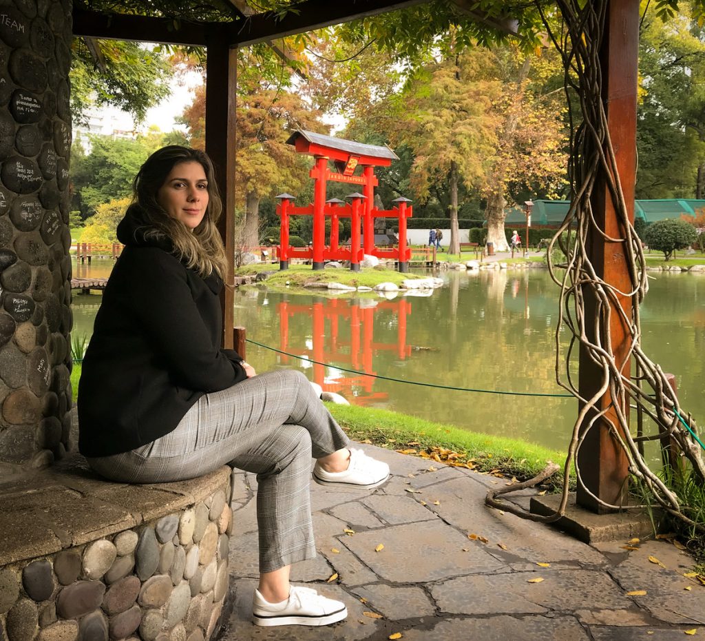 Mulher sentada em banco com lago e portal japonês ao fundo.