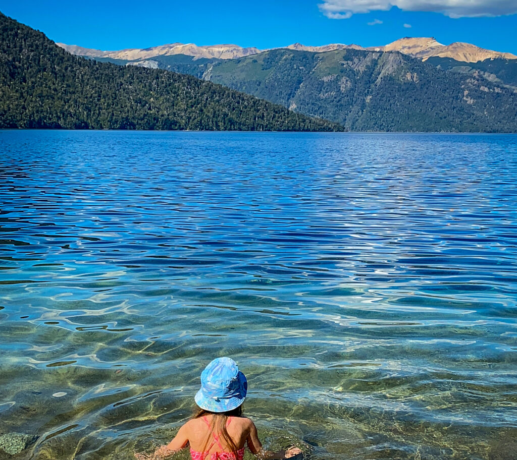 menina de costas em lago cristalino com montanhas