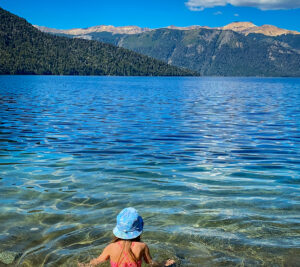 menina de costas em lago cristalino com montanhas