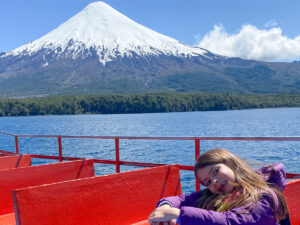 menina em banco de barco navegando no lago com vulcão com neve ao fundo