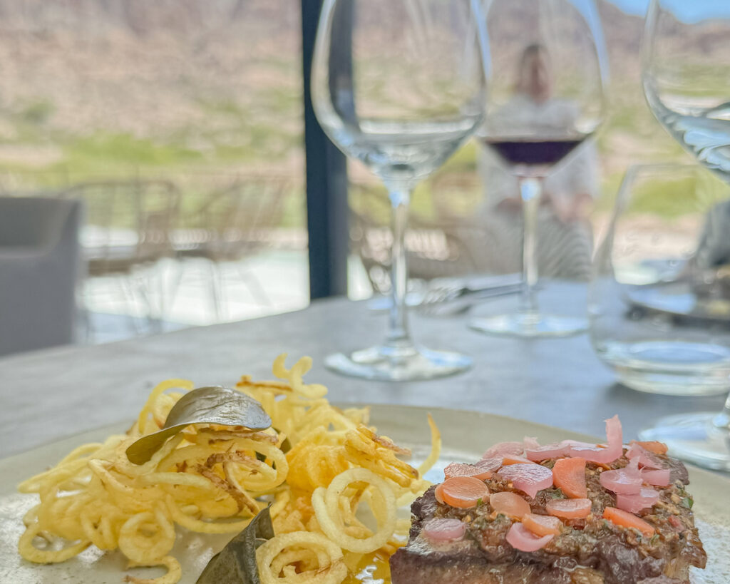 prato com carne com taças de vinho e paisagem de montanha ao fundo