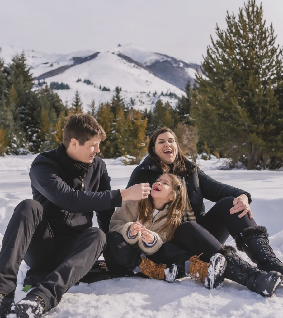 familia de pai, mãe e menina sentandos brincando na neve