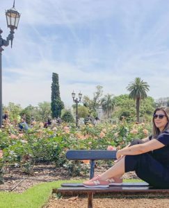 mulher sentada de lado em banco de parque de rosas