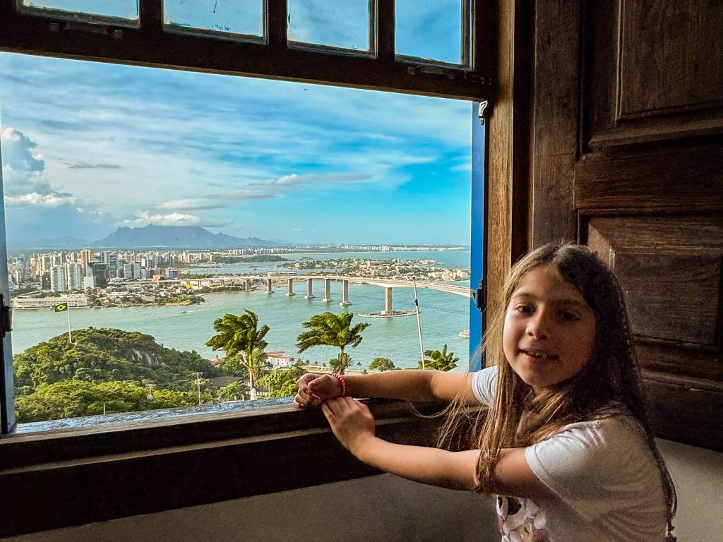 menina em janela com vista para mar e ponte