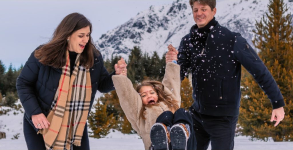 mãe e pai segurando menina um em cada braço brincando na neve