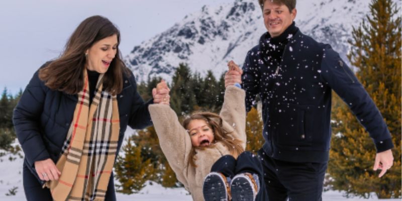 mãe e pai segurando menina um em cada braço brincando na neve