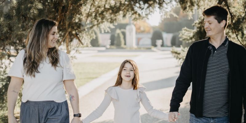 mãe, filha e pai e de mãos dadas andando em parque