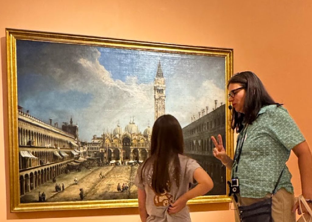 menina vendo quadro em museu com guia de turismo ao lado