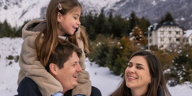 menina em "cangote" do pai e mãe olhando para eles com paisagem de neve ao fundo