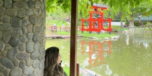 mulher sentada em banco olhando lago e tori japonês ao fundo