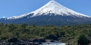 vulcão nevado ao fundo com mata e rio de pedras a frente